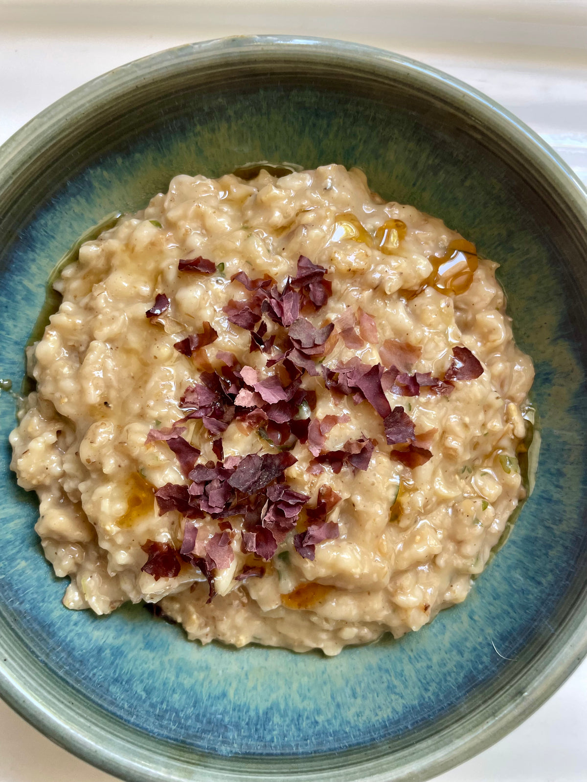 A close up shot of creamy savory mushroom oatmeal topped with dulse flakes and drizzle of sesame oil